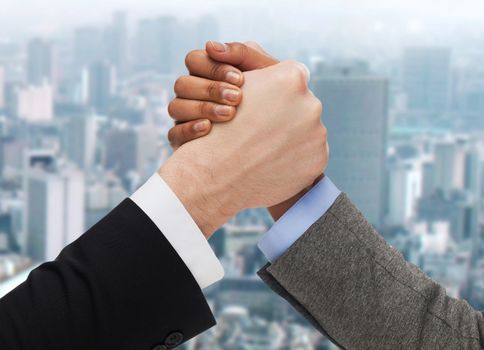 business, people and competition concept - close up of two people hands arm wrestling over ciity background