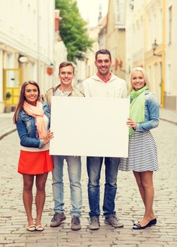 travel, vacation and advertising concept - group of smiling friends with blank white board in the city