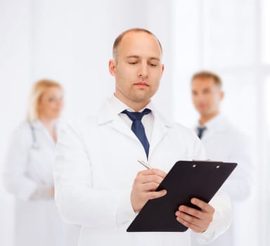 medicine, profession, teamwork and healthcare concept - serious male doctor with clipboard writing prescription over group of medics