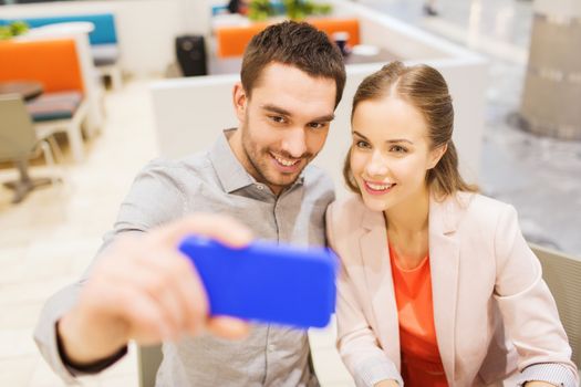 technology and people concept - happy couple taking selfie with smartphone in mall or cafe