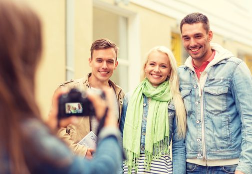 travel, vacation, technology and friendship concept - girl picturing group of friends with map and city guide in city