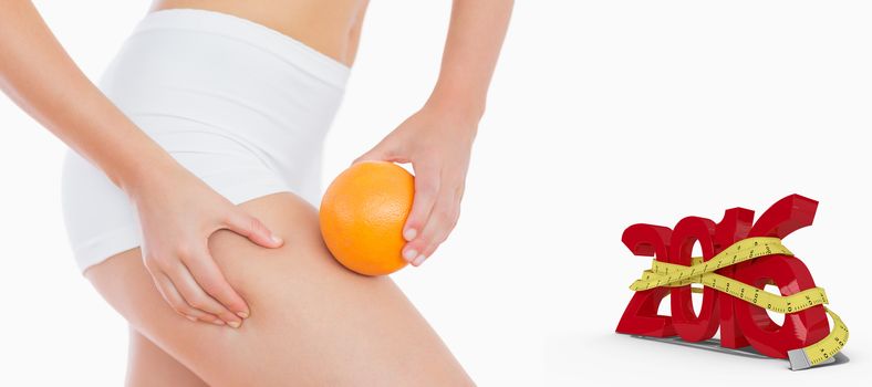 Woman squeezing fat on thigh as she holds orange against white background with vignette