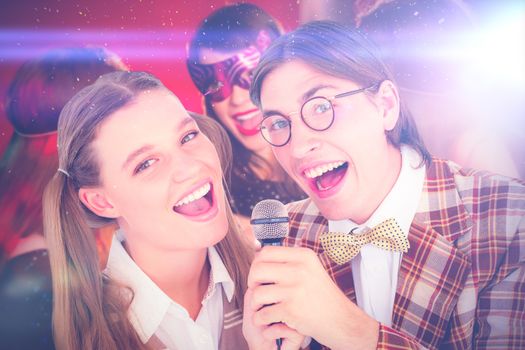 Happy geeky hipsters singing with microphone against friends in masquerade masks drinking champagne