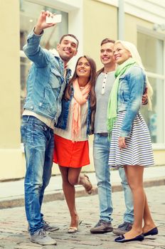 travel, vacation, technology and friendship concept - group of smiling friends making selfie with smartphone camera outdoors