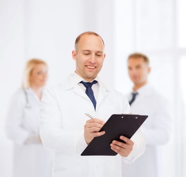 medicine, profession, teamwork and healthcare concept - smiling male doctor with clipboard writing prescription over group of medics