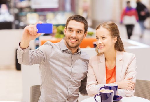 sale, shopping, consumerism, technology and people concept - happy young couple with smartphone taking selfie at cafe in mall