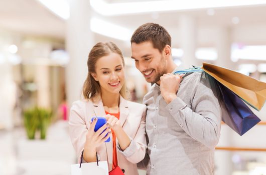 sale, consumerism, technology and people concept - happy young couple with shopping bags and smartphone talking in mall