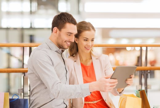 sale, consumerism, technology and people concept - happy young couple with shopping bags and tablet pc computer in mall