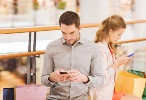 sale, consumerism, technology and people concept - young couple with shopping bags and smartphones in mall