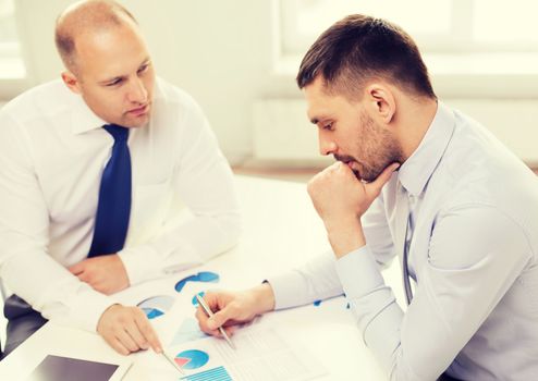 business, technology and office concept - two businessmen with tablet pc computer and papers having discussion in office