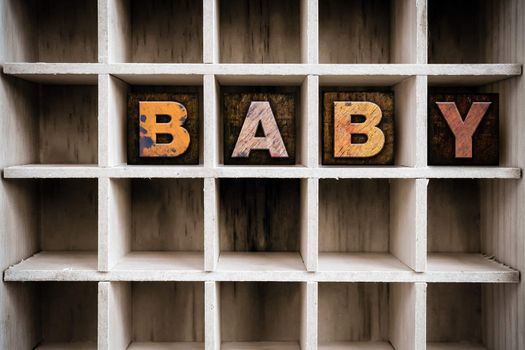 The word "BABY" written in vintage ink stained wooden letterpress type in a partitioned printer's drawer.