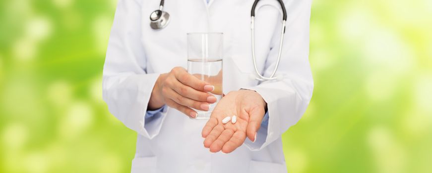 healthcare, medicine, people and pharmacy concept - close up of doctor with stethoscope offering pills and water over green background