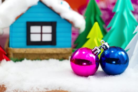 Pink and blue christmas ball on snow and christmas tree with little house.