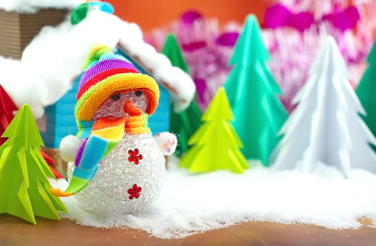 Snowman on snow with christmas tree and small house background.