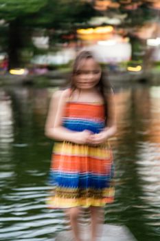 Young girl in colorful dress by lake, defocused