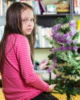 Young girl decorating Christmas tree looking at camera