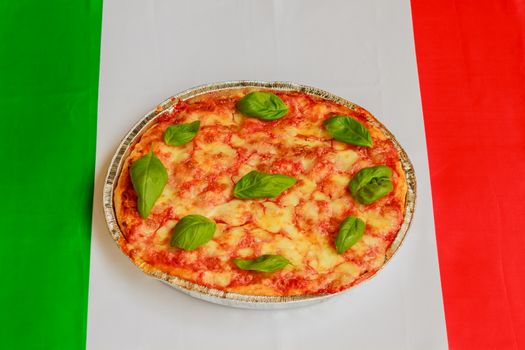 typical italian pizza  made of tomato,basil and mozzarella with the italian flag in the background