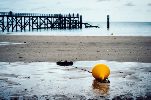 Orange buoy on a beach, pier in the background in Noirmoutier, France. Film emulation filter applied.