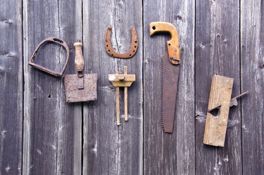 Old rusty tools hanging on grey wooden farm barn wall