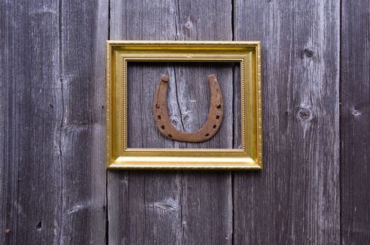 Golden ornate frame with rusty horseshoe on wooden wall