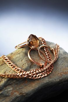 Gold ring and chain on gray stone against nice dark background