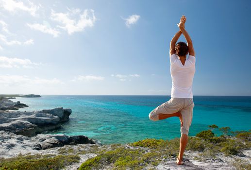fitness, sport, people and lifestyle concept - young man making yoga exercises on beach from back
