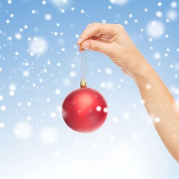 christmas, decoration, holidays and people concept - close up of woman hand holding christmas ball over blue background with snow