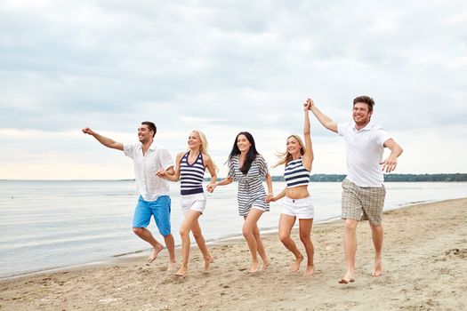 summer, holidays, sea, tourism and people concept - group of smiling friends in sunglasses running on beach