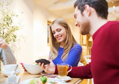 people, leisure, friendship and technology concept - smiling couple with smartphones meeting and drinking tea at cafe