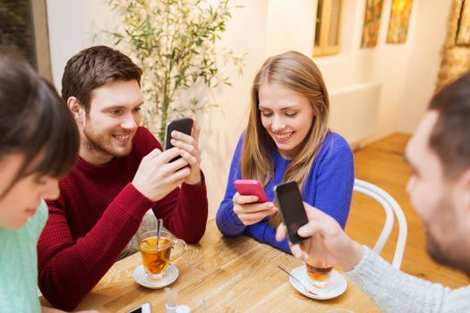 people, leisure, friendship and technology concept - group of happy friends with smartphones meeting at cafe and drinking tea