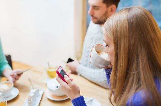 people, leisure, friendship and technology concept - couple with smartphones meeting and drinking tea at cafe