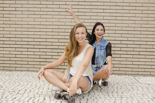 Two beautiful and young girlfriends having fun with a skateboard