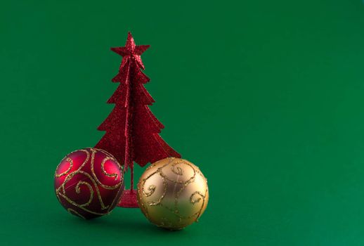 Little, red metallic christmas tree with tree adornments on green background