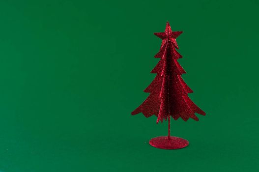 Little, red metallic christmas tree on green background