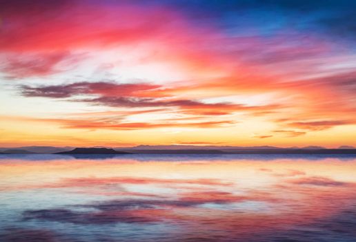 sunset scene on quiet sea with mountains in background, colorful sky with soft clouds