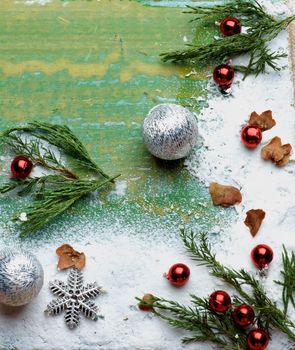 Handmade Christmas Greeting Theme with Border of Green Branches, Snow Flakes, Silver Baubles and Red Bead closeup on Cracked Wooden background