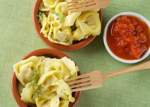 Delicious Meat Cappelletti with Herbs, Tomatoes Sauce and Wooden Forks closeup on Green Napkin background. Top View