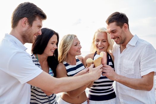 summer, holidays, sea, tourism and people concept - group of smiling friends eating ice cream on beach