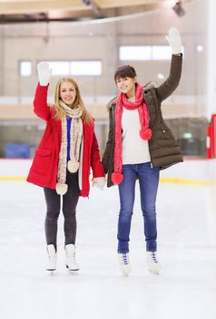 people, women, friendship, sport and leisure concept - two happy girls friends waving hands on skating rink