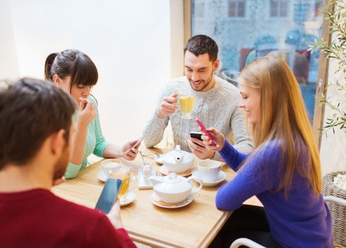 people, leisure, friendship and technology concept - group of happy friends with smartphones meeting at cafe and drinking tea