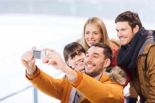 people, friendship, technology and leisure concept - happy friends taking selfie with digital camera on skating rink