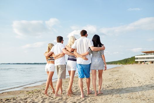 summer, holidays, sea, tourism and people concept - group of smiling friends hugging and walking on beach from back