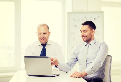 business, technology and office concept - two smiling businessmen with laptop in office