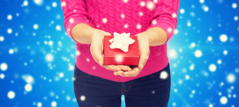 christmas, holidays and people concept - close up of woman in pink sweater holding gift box blue snowy background