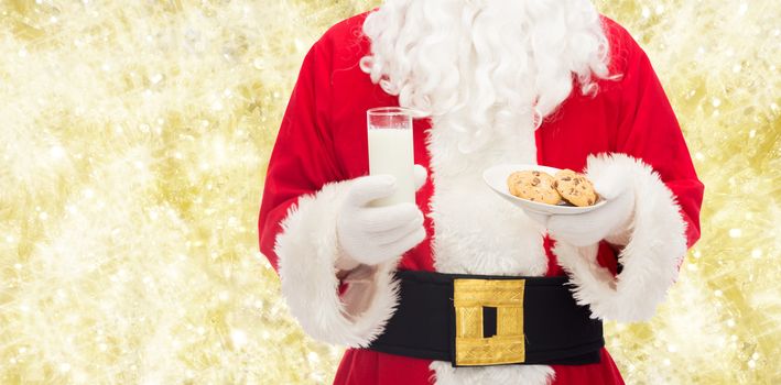 christmas, holidays, food, drink and people concept -close up of santa claus with glass of milk and cookies over yellow lights background