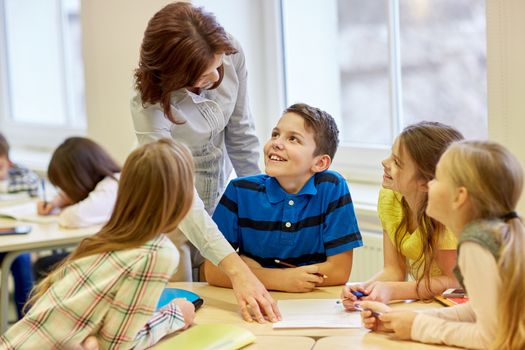 education, elementary school, learning and people concept - teacher helping school kids writing test in classroom