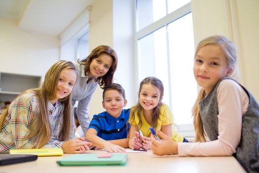 education, elementary school, learning and people concept - teacher helping school kids writing test in classroom