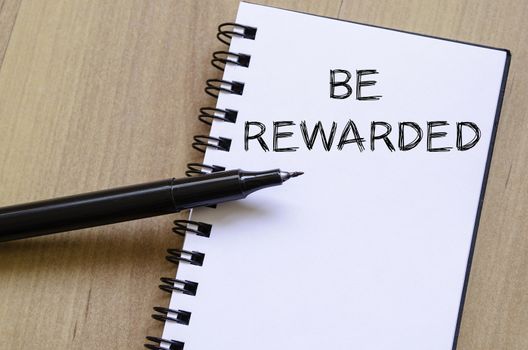 Be rewarded text concept write on notebook with pen