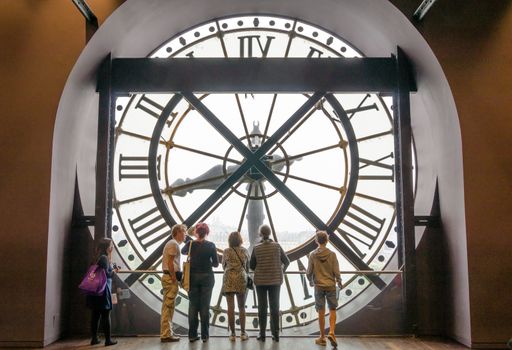 Paris, France - May 14, 2015: Unidentified tourists looking through the clock with roman numerals in the museum D'Orsay. The museum houses the largest collection of impressionist and post-impressionist masterpieces in the world.