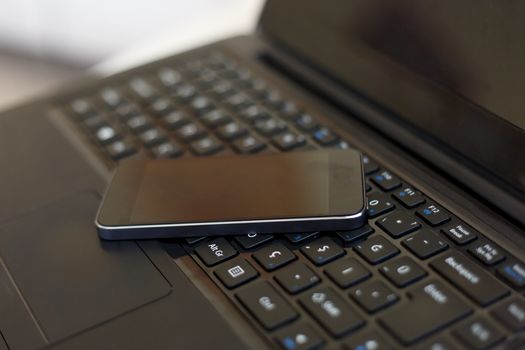 Close up detailed view of a black laptop pc with a black smart phone on.
